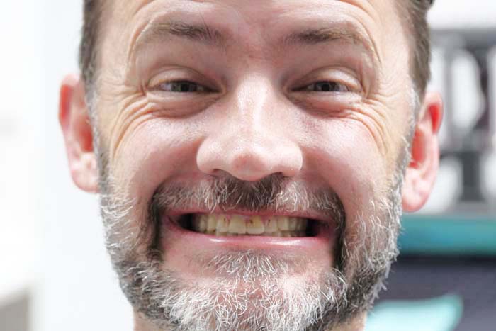 The image shows a man with facial hair and a mustache, wearing glasses, smiling broadly at the camera.