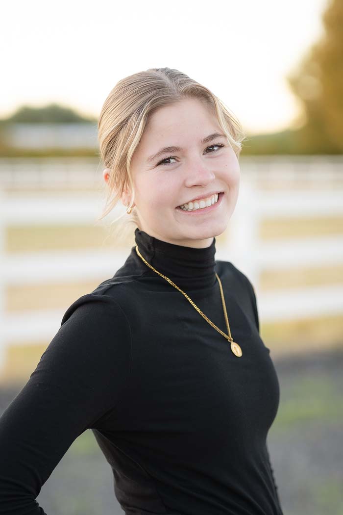 The image shows a woman smiling at the camera while standing outdoors during daylight.