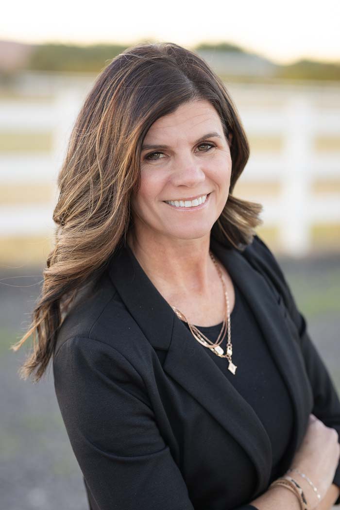 Woman standing outdoors with a white fence behind her.
