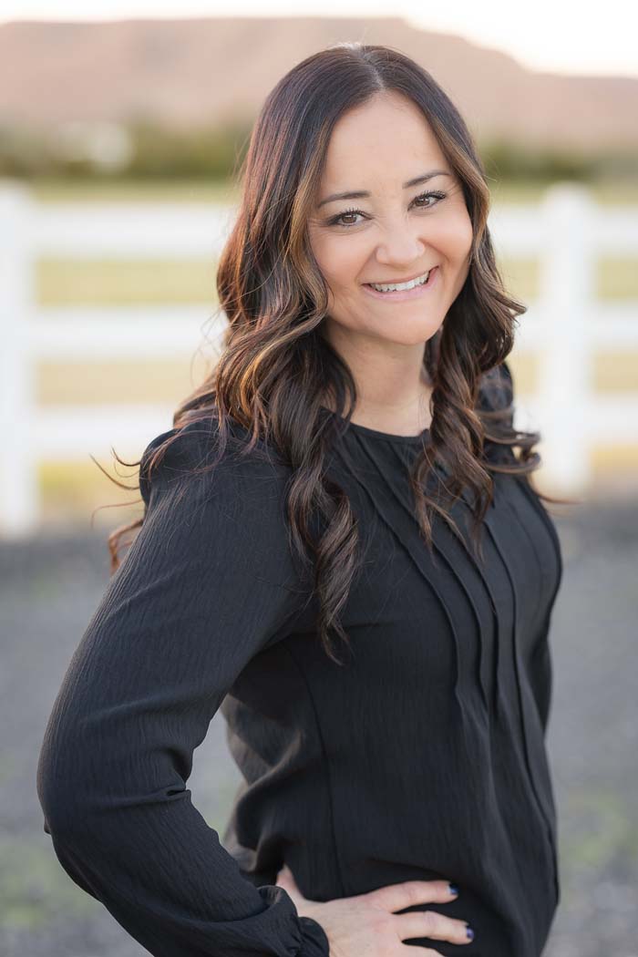 The image depicts a woman standing outdoors with a fence in the background, smiling at the camera.